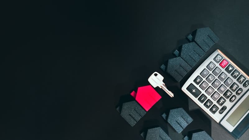 Small house model, a key and a calculator on a dark surface