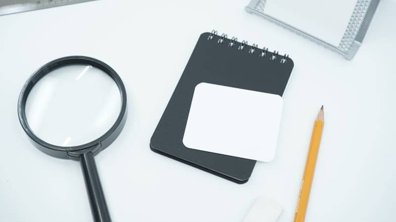 Magnifying glass beside a notepad and pencil on a white surface