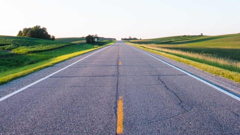 Straight empty road running between green fields
