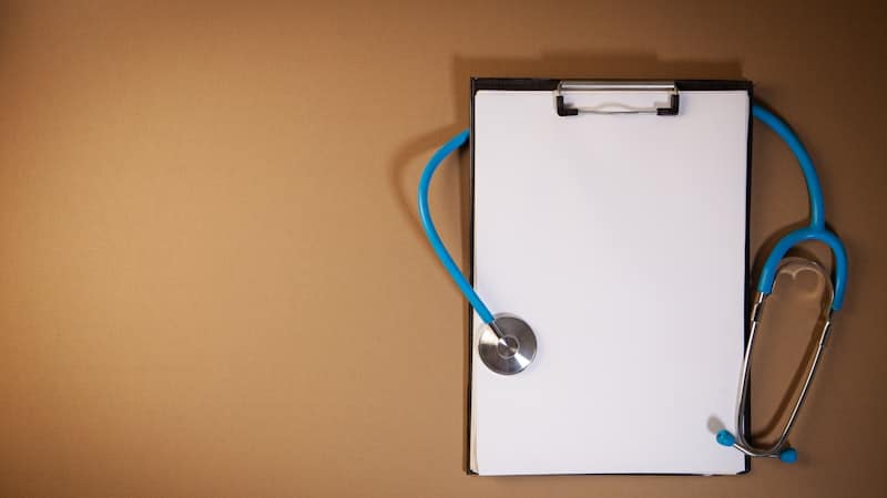 Clipboard with a blank page and a stethoscope on a brown surface